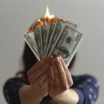 A woman holding burning 100 dollar bills